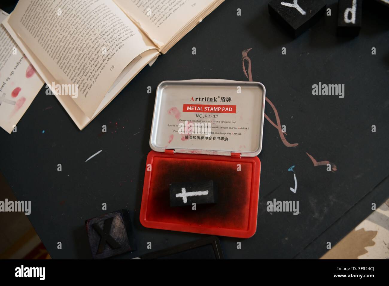 Une vue aérienne d'un bureau de couleur sombre met en scène un livre ouvert avec du texte, un tampon encreur rouge ouvert et plusieurs tampons à lettres noirs éparpillés autour. Banque D'Images