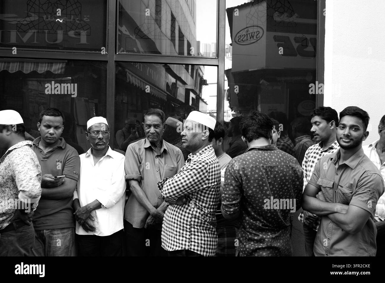 Dubaï - Émirats- 2019 : Photographie de rue en noir et blanc candide capturant un groupe d'hommes debout devant une boutique dans une zone urbaine animée. Banque D'Images
