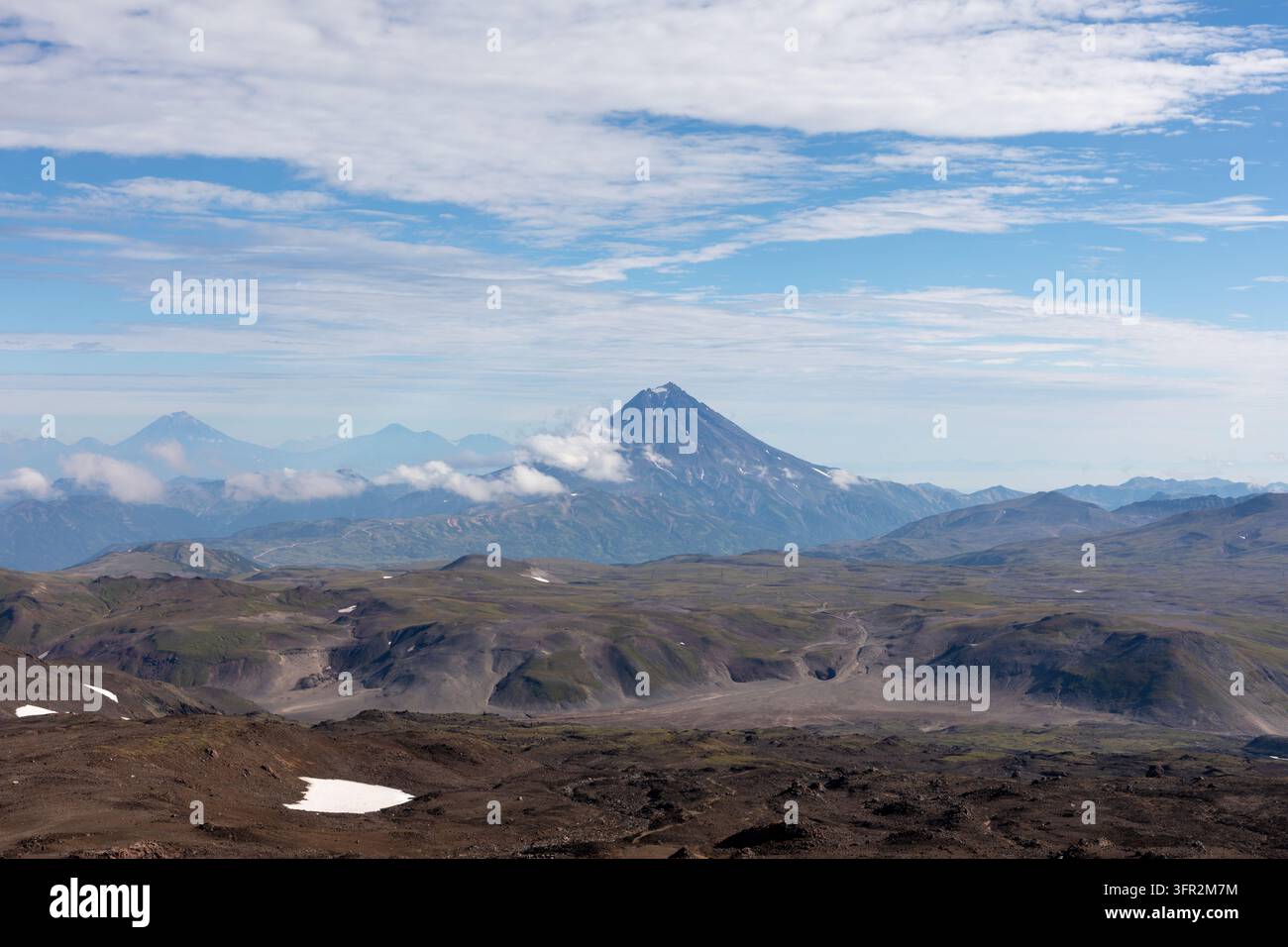 Stratovolcan majestueux s'élevant au-dessus de la vallée volcanique avec un terrain rocheux, des plaques de neige et un ciel bleu au kraï de Kamtchatka, en Russie, montrant une vue à couper le souffle Banque D'Images