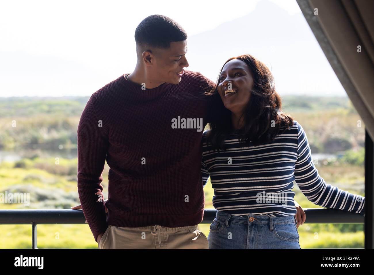 Couple afro-américain appuyé sur la rambarde métallique d'un balcon, souriant, portant un pull en tricot, un haut rayé Banque D'Images