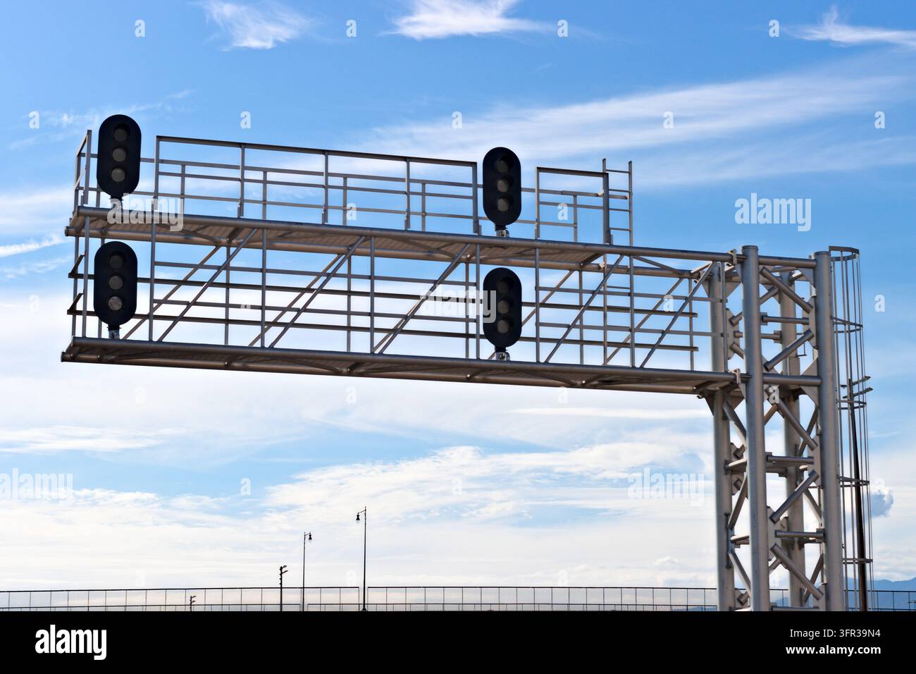 Un grand portique en acier pour signal ferroviaire avec quatre têtes de signal éteintes, des passerelles surélevées et une échelle d'accès se dresse contre un ciel bleu parsemé de légers nuages blancs Banque D'Images