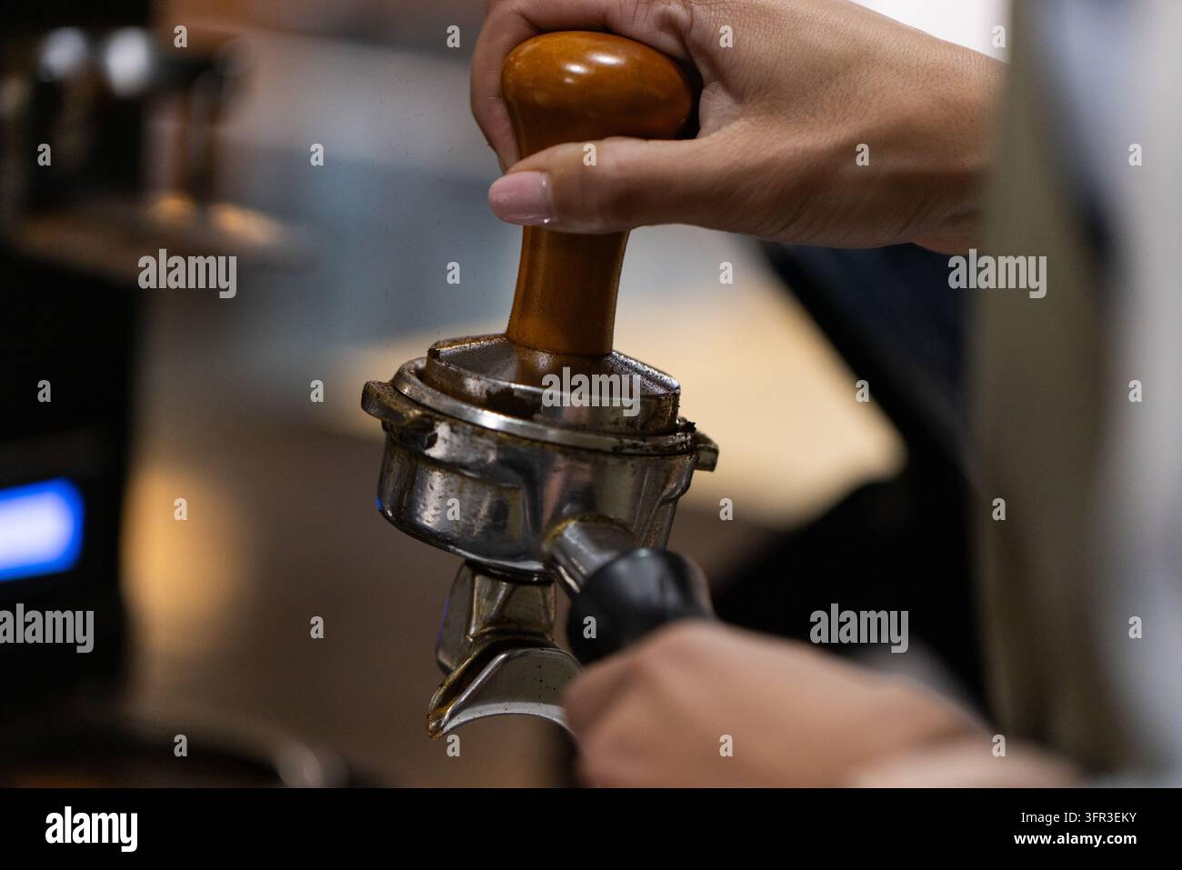 Barista asiatique d'âge moyen tassant le marc de café avec un tamper dans le porte-filtre près de la machine à expresso Banque D'Images