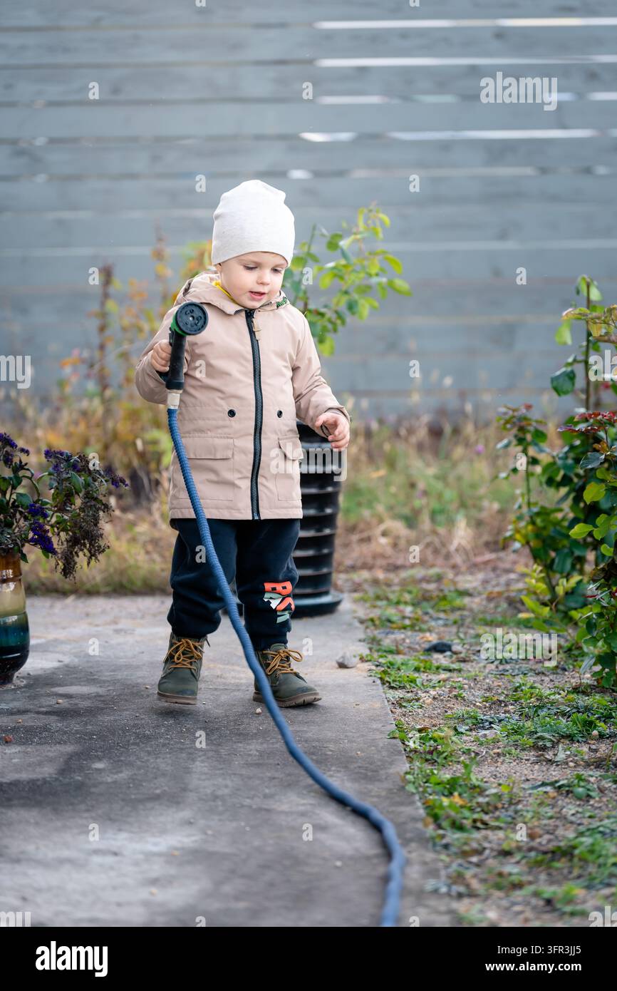Garçon arrosant un rosier lors de l'entretien automnal dans le jardin fleuri de l'arrière-cour Banque D'Images