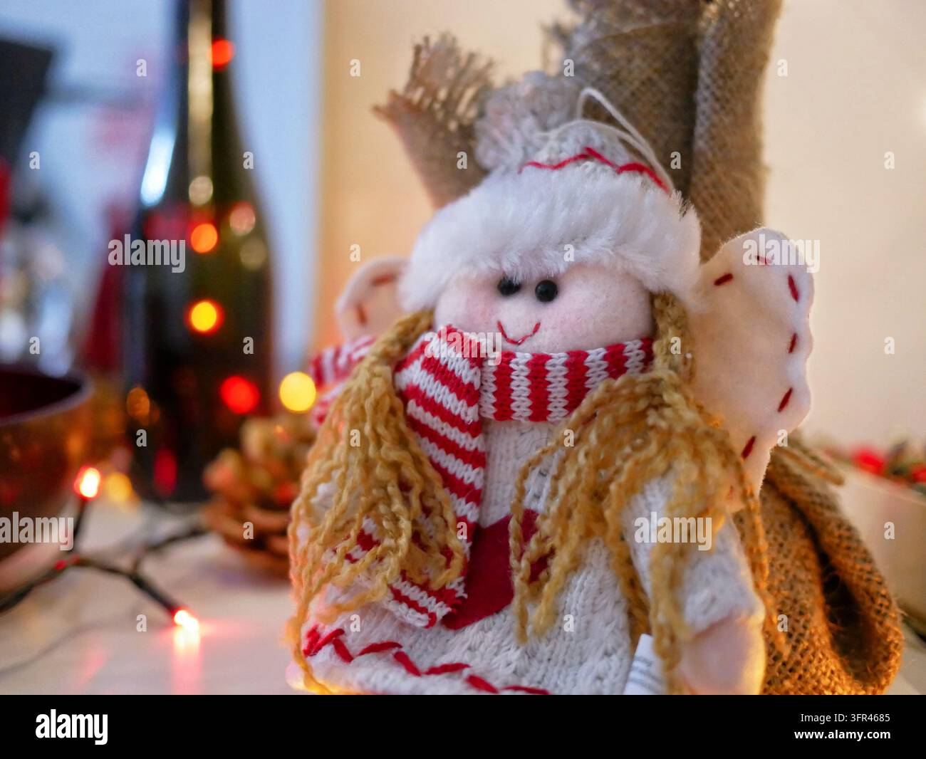Close-up d'une poupée ange de Noël faite à la main portant une écharpe rayée rouge et blanc et une tenue tricotée avec des guirlandes lumineuses chaudes Banque D'Images