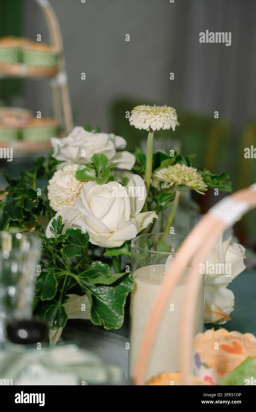 Centre de table élégant en roses blanches et une bougie dans un porte-bougie en verre sur une table de fête Banque D'Images