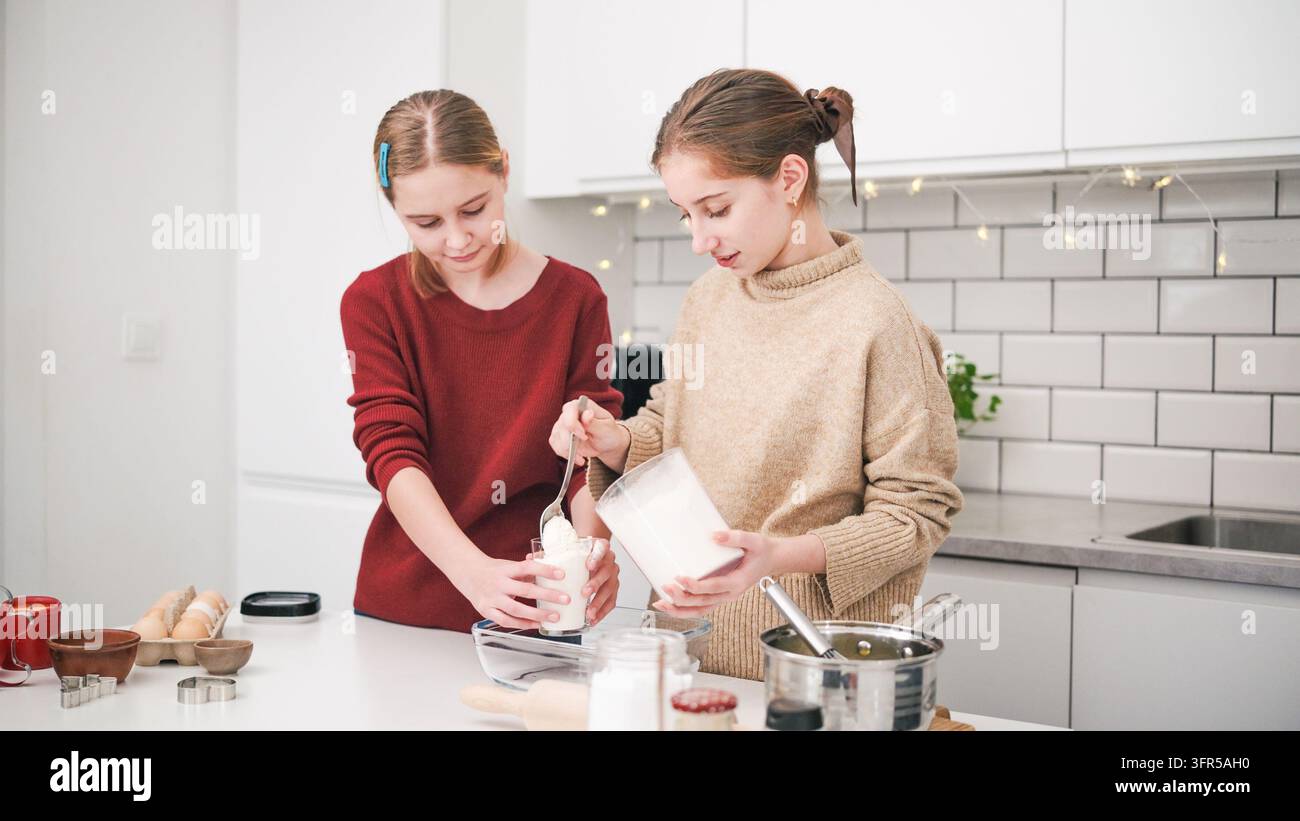 Sœurs cuisinent des biscuits gingersnaps pour Noël, versant de la farine dans le mélange de pâte Banque D'Images