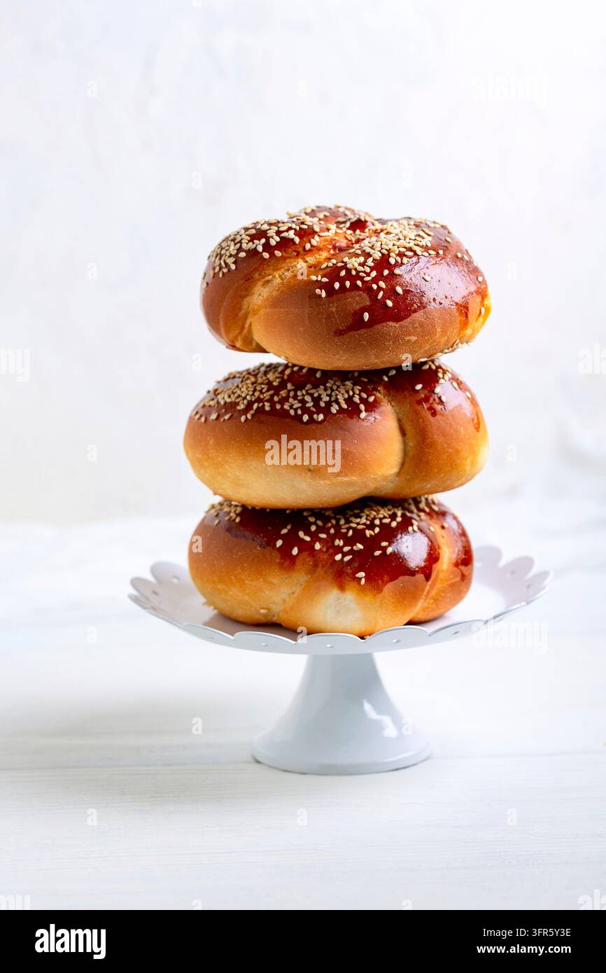 Pile de petits pains ronds sucrés à la levure, type challah, avec graines de sésame dans un support métallique vintage sur fond clair. Concept de pâtisserie festive Banque D'Images