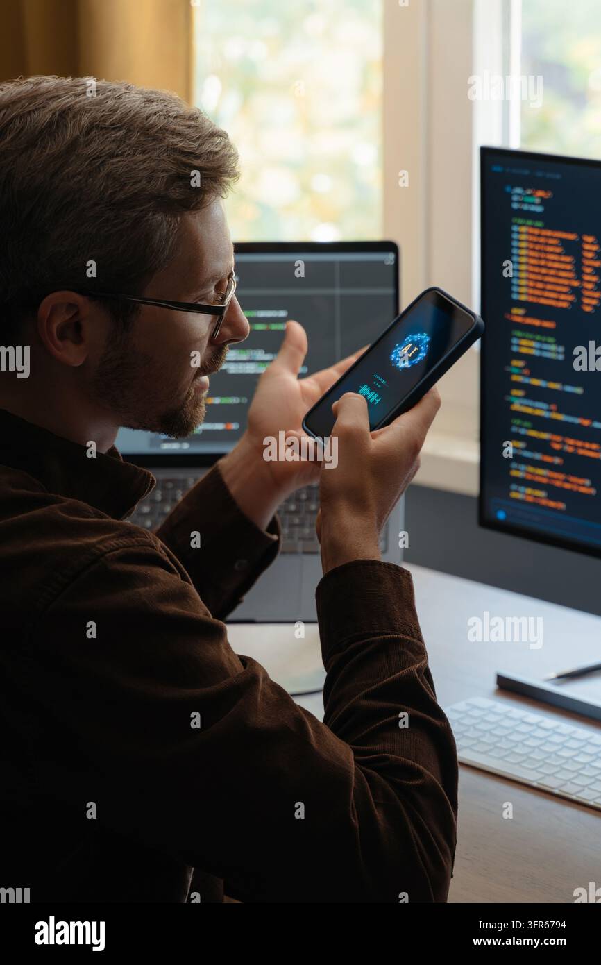 Programmeur communiquant avec un agent IA via un smartphone, utilisant un assistant numérique vocal sur le téléphone pour le développement logiciel et le codage vibe. Homme parlant avec une application alimentée par l'intelligence artificielle Banque D'Images