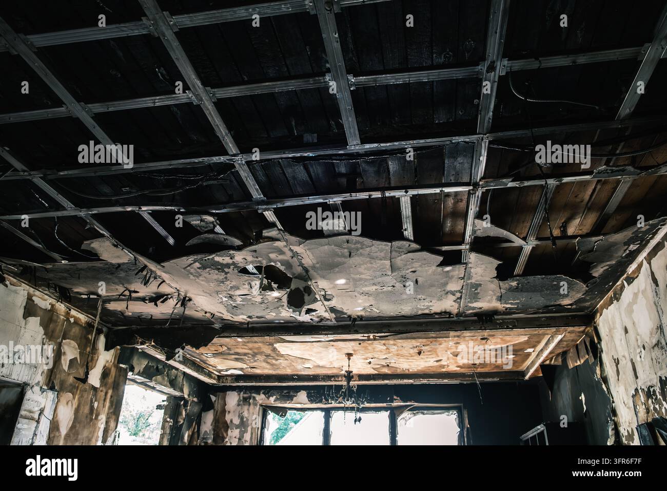 Une pièce intérieure montre un plafond fortement endommagé par le feu avec une grille métallique exposée, des panneaux manquants et des traces de carbonisation et de fumée visibles, destruction Banque D'Images