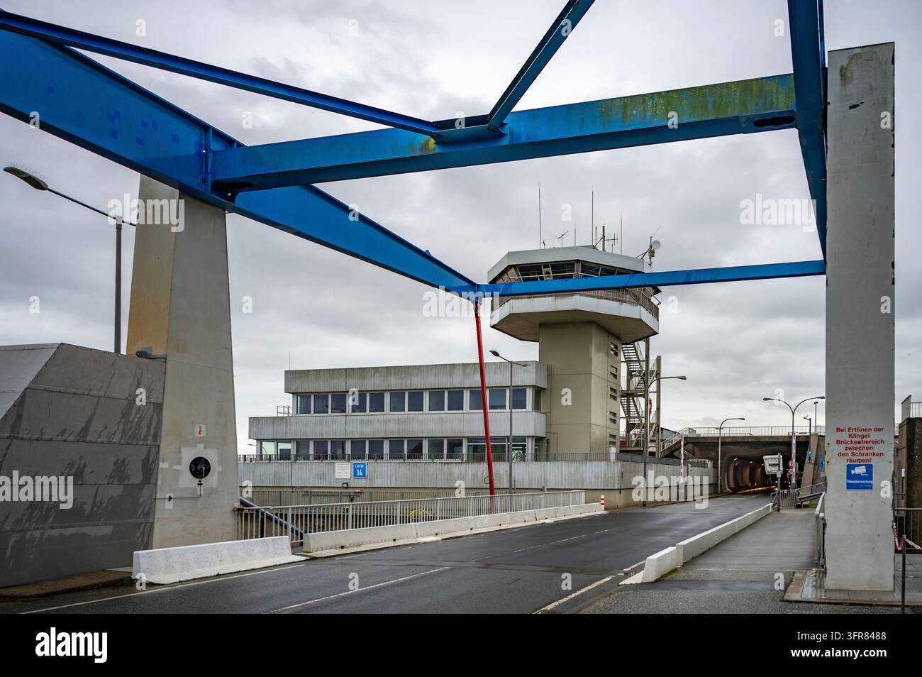 Une tour de contrôle se dresse à l'arrière-plan d'un pont avec une structure bleue au-dessus, menant à un bâtiment, Eidersperrwerk, mer du Nord, Allemagne Banque D'Images