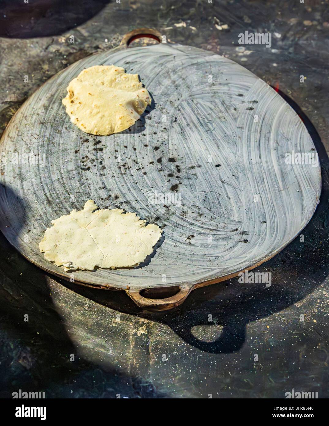Vue aérienne de deux tortillas de maïs faites à la main cuisant sur une plaque traditionnelle (comal) à Ek Balam, Yucatan, Mexique. Les galettes de masa non cuites reposent sur un M usé Banque D'Images