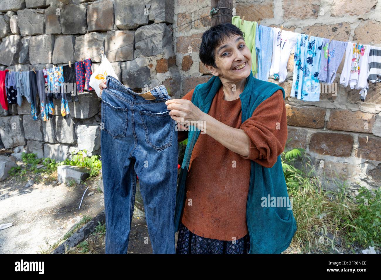Femme souriante tenant un jean devant du linge séchant sur une corde contre un mur de pierre, Erevan, Erevan, Arménie Banque D'Images