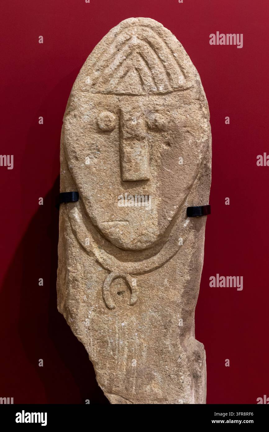Un ancien idole en pierre sculpté avec un visage et un collier est exposé contre un mur rouge dans un musée, à Erevan, Erevan, Arménie Banque D'Images