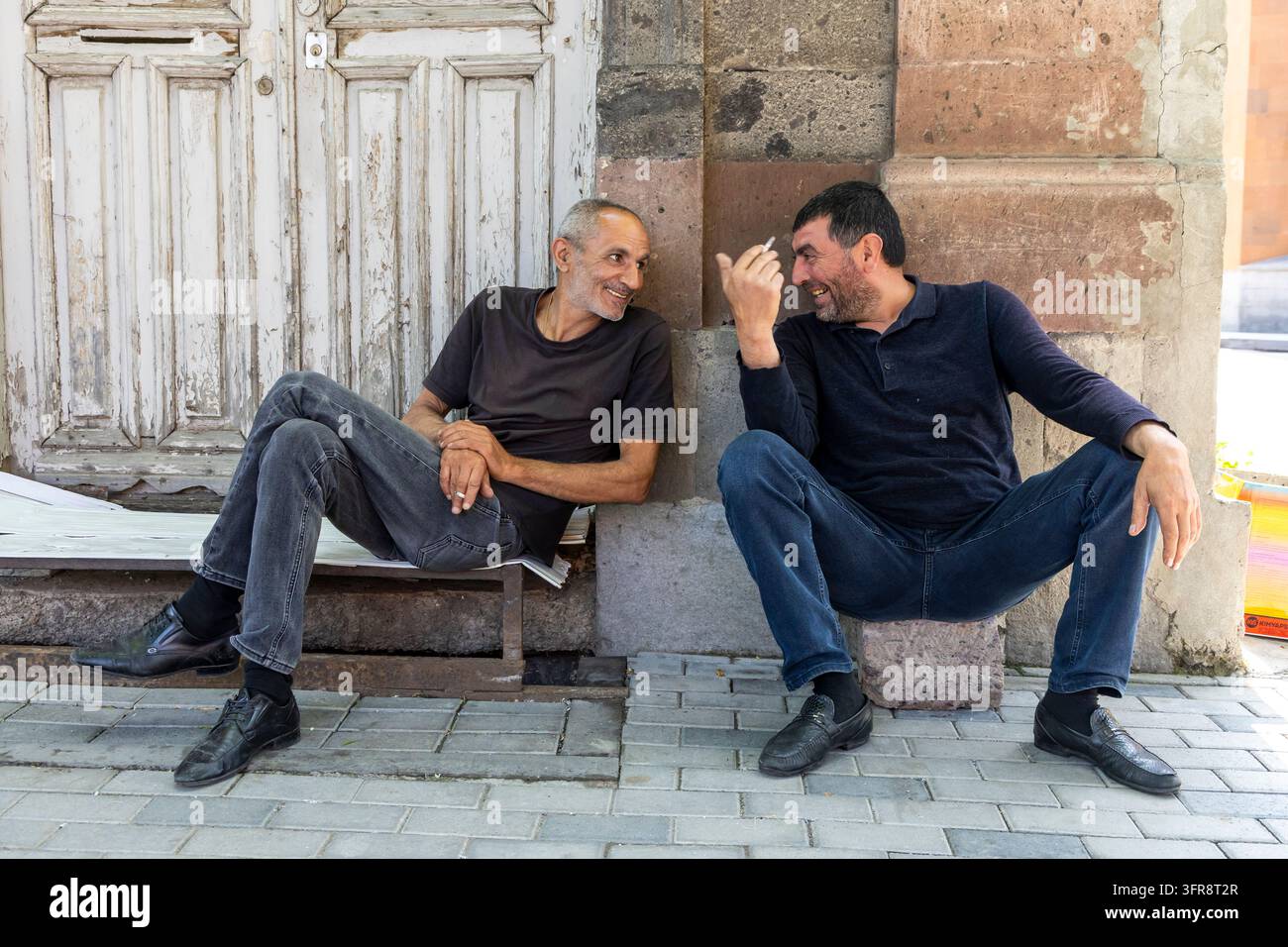 Deux hommes âgés discutant et fumant assis sur un banc devant une vieille porte en bois, province de Shirak, Gyumri, Arménie Banque D'Images