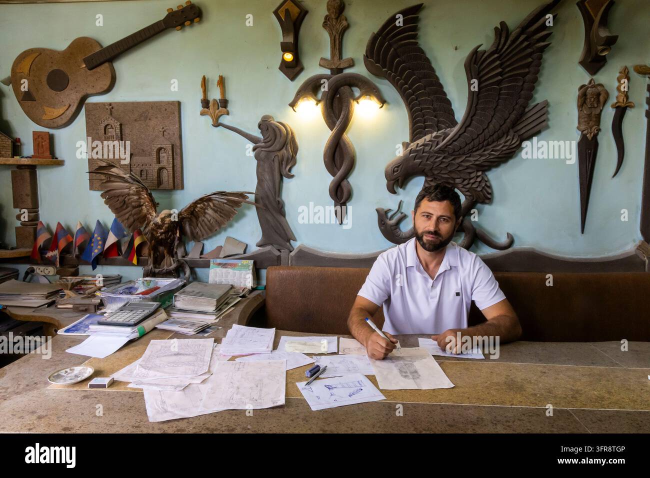 Sculpteur sur bois assis à son bureau entouré de sculptures taillées dans son atelier, province de Gegharkunik, Noratus, Arménie Banque D'Images