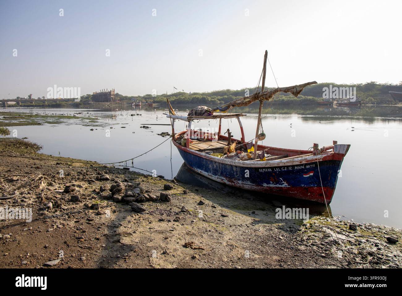 Un bateau de pêche en bois coloré est amarré le long de la rive avec une chantier naval visible au loin, Gujarat, Mandvi, Inde Banque D'Images