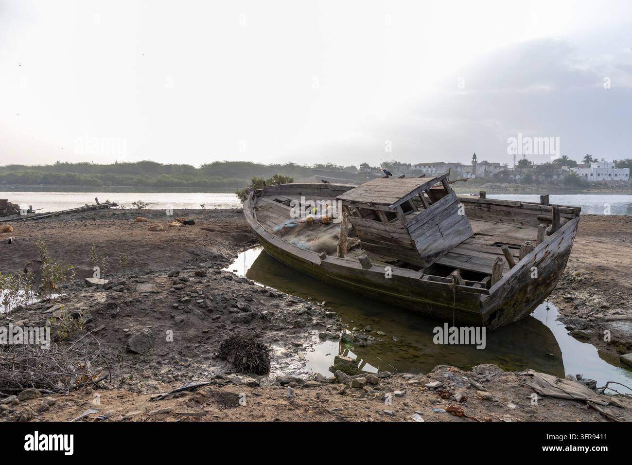 Un bateau de pêche en bois abandonné gît échoué sur une rive boueuse près d'une ville côtière, Gujarat, Mandvi, Inde Banque D'Images