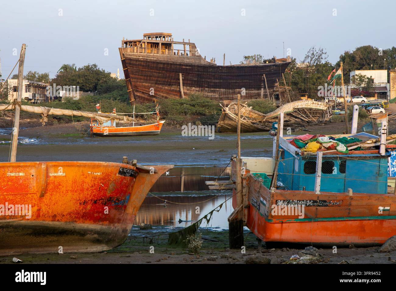 Des bateaux de pêche colorés reposent près d'un grand dhow en bois en construction dans un chantier naval animé, Gujarat, Mandvi, Inde Banque D'Images
