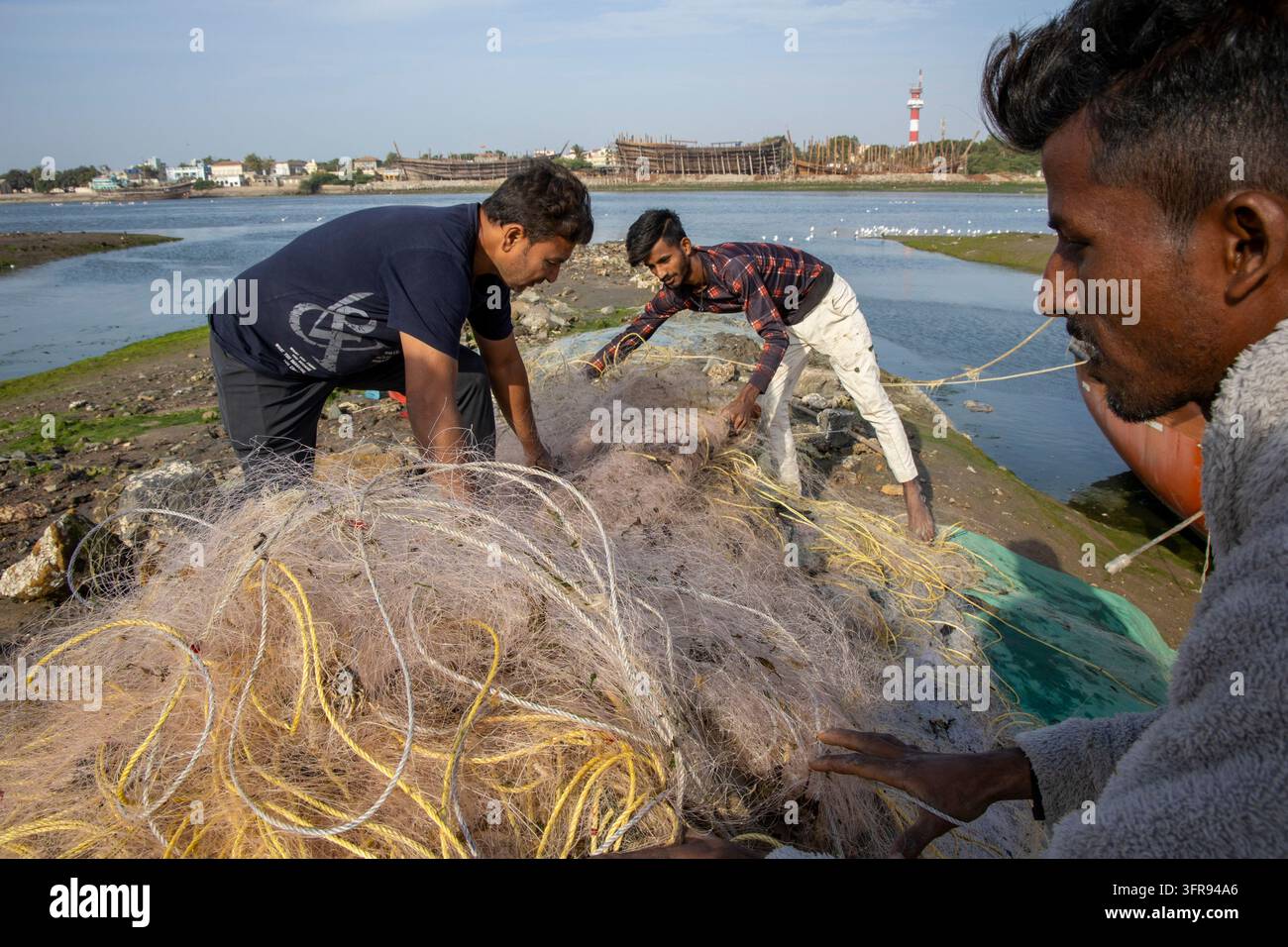 Groupe de pêcheurs démêlant un grand filet de pêche sur la rive près d'une chantier naval, Gujarat, Mandvi, Inde Banque D'Images