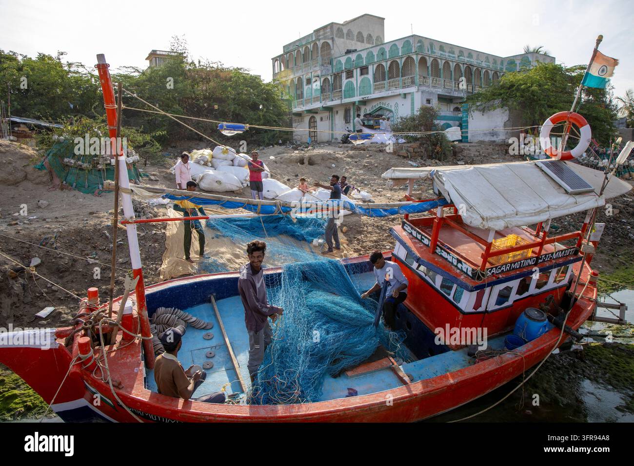 Pêcheurs triant des filets de pêche bleus à bord d'un bateau avec un manoir orné en arrière-plan, Gujarat, Mandvi, Inde Banque D'Images