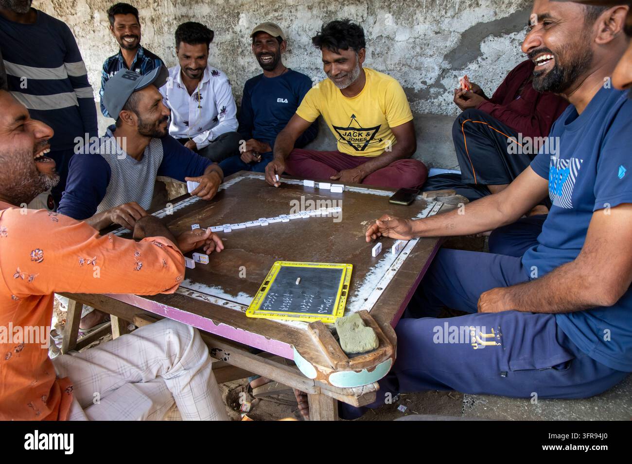 Groupe d'hommes riant en jouant au domino sur une table en bois sous un abri, Gujarat, Mandvi, Inde Banque D'Images