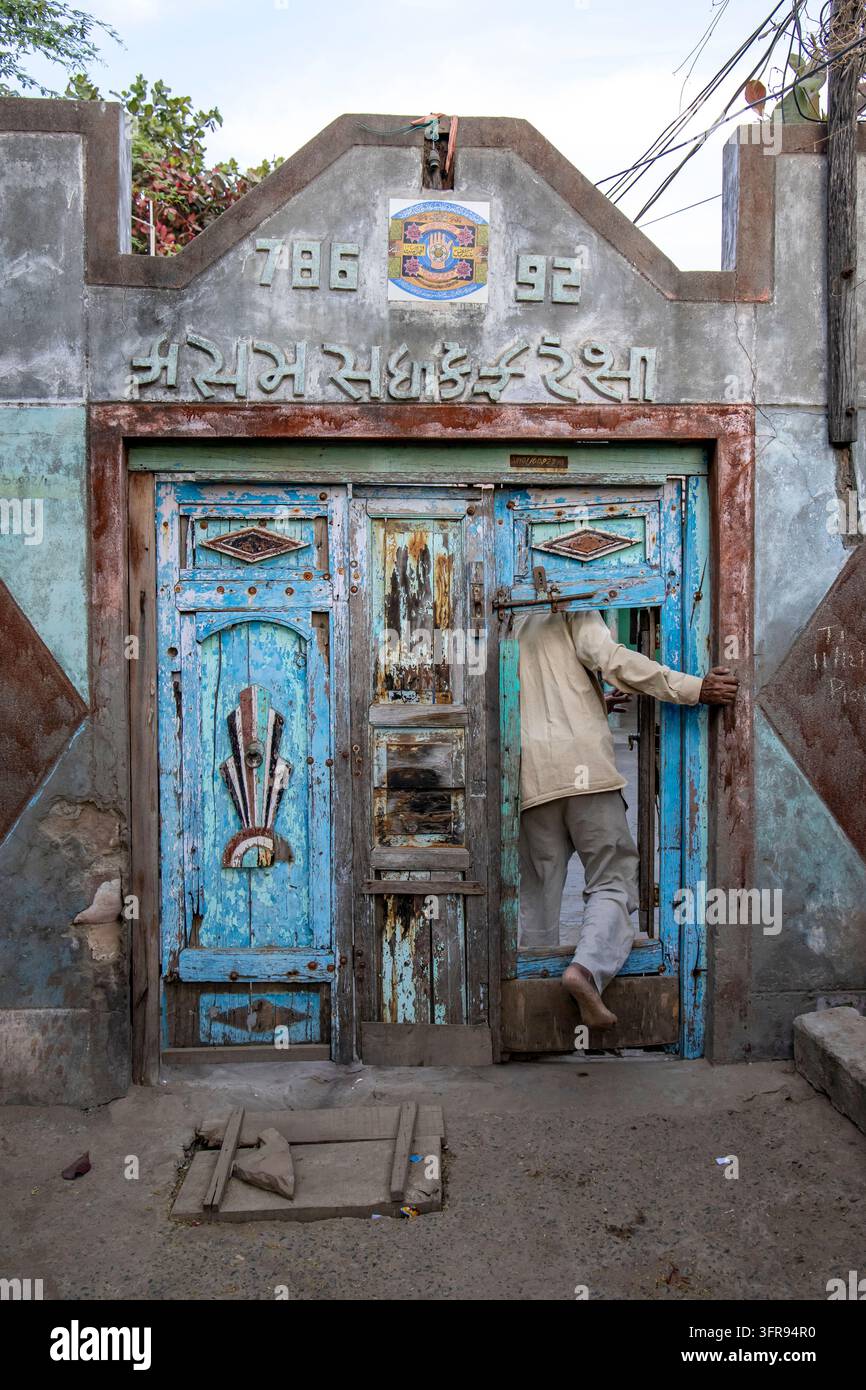Homme vêtu de blanc franchissant une porte en bois bleu patiné ornée d'une inscription gujarati, Gujarat, Mandvi, Inde Banque D'Images