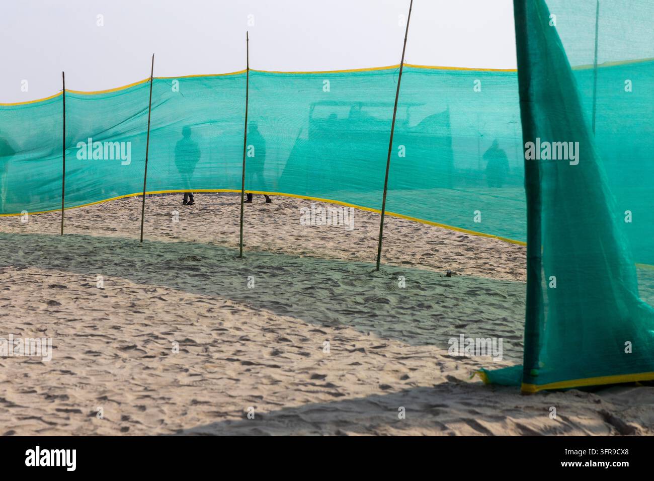 Filet d’ombrage vert sur le sable avec des silhouettes de personnes marchant derrière à la Maha Kumbh Mela, Uttar Pradesh, Prayagraj, Inde Banque D'Images