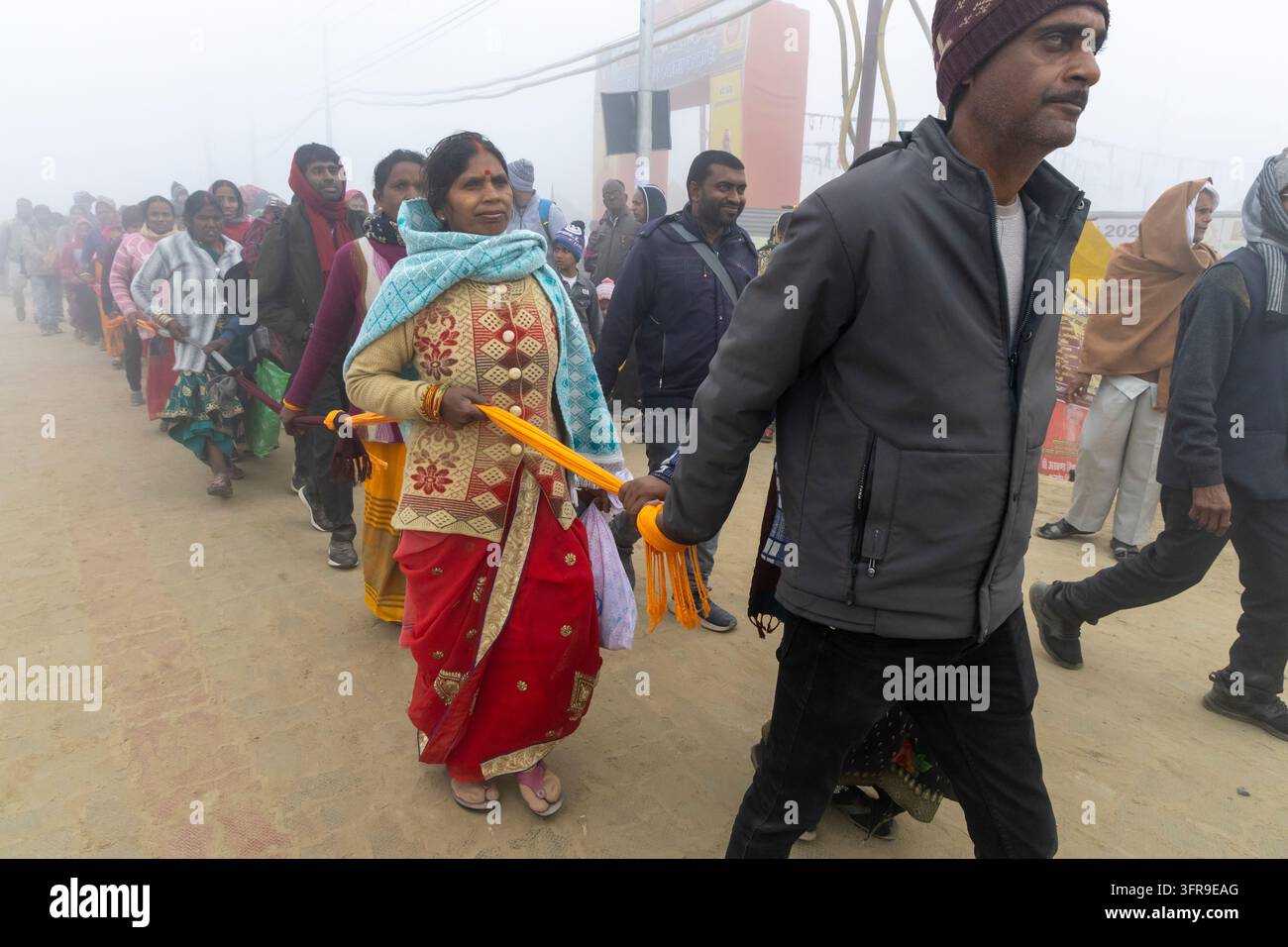 Hommes et femmes attachés ensemble par une corde jaune marchant en longue file à travers le brouillard lors du Maha Kumbh Mela, Uttar Pradesh, Prayagraj, Inde Banque D'Images