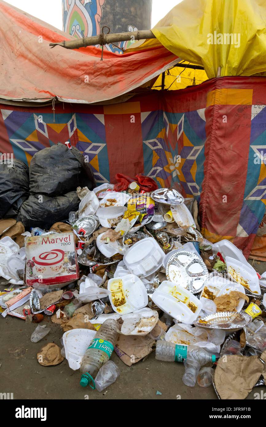 Pile d'assiettes, de tasses, de bouteilles et de sacs usagés devant un mur de tente coloré à la Maha Kumbh Mela, Uttar Pradesh, Prayagraj, Inde Banque D'Images