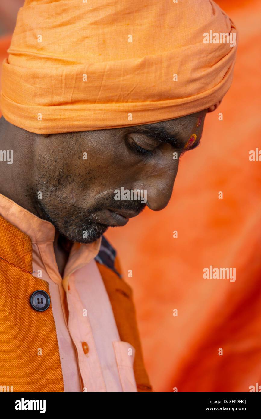 Close-up d'un homme portant un turban et une veste orange, regardant vers le bas avec un tilak sur le front à la Maha Kumbh Mela, Uttar Pradesh, Prayagraj, Inde Banque D'Images