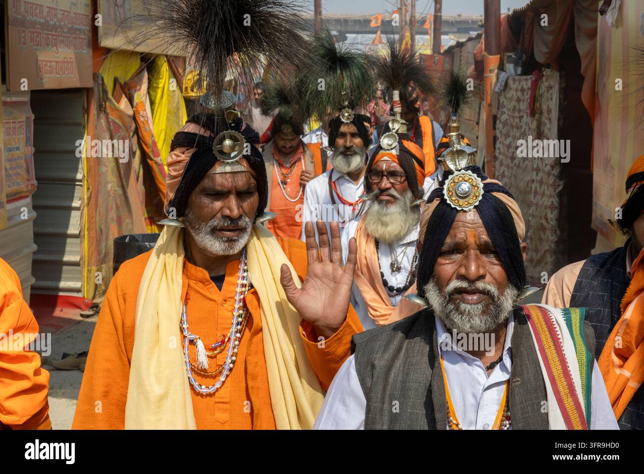 Des sadhus barbus vêtus d'oranges et de turbans noirs ornés de plumes défilent en procession dans une allée du camp, Uttar Pradesh, Prayagraj, Inde Banque D'Images