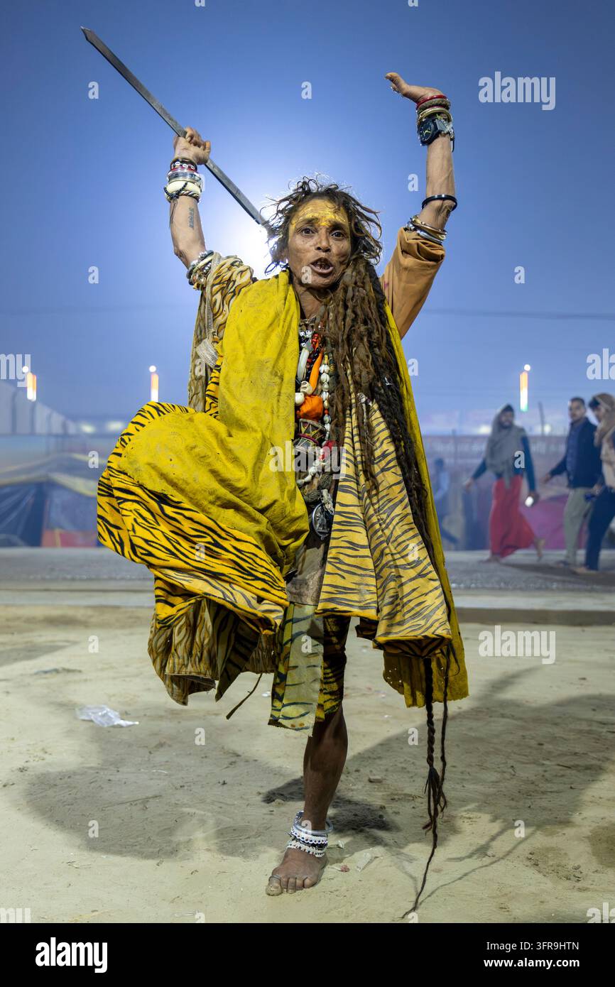 Sadhu aux longues dreadlocks et au tissu à motif tigre jaune danse avec une épée levée lors du Maha Kumbh Mela, Uttar Pradesh, Prayagraj, Inde Banque D'Images