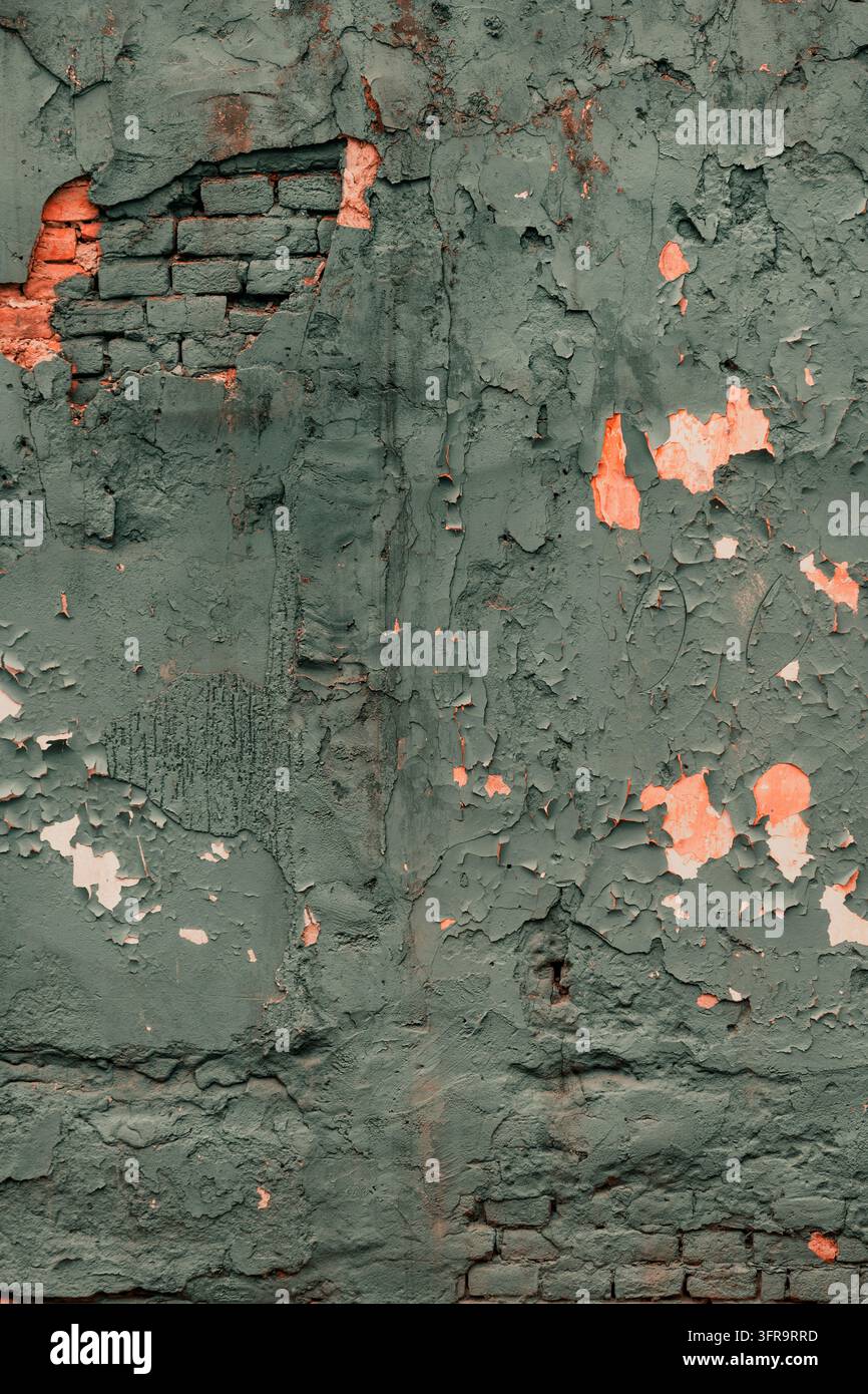 Mur érodé avec un enduit gris-vert fissuré, de la peinture écaillée et de la brique rouge apparente. Texture architecturale usée idéale pour les arrière-plans grunge Banque D'Images