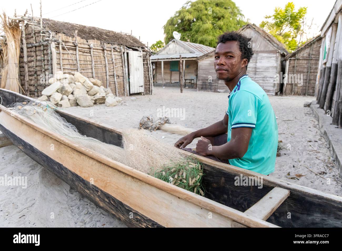 Un pêcheur Vezo est assis dans sa pirogue en bois et répare soigneusement un filet de pêche dans la cour de sable du village, Menabe, Belo sur Mer, Madagascar Banque D'Images