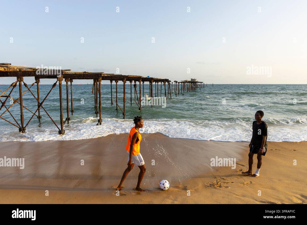 Deux jeunes hommes jouant au football sur la plage à côté des restes rouillés d'un vieux quai, Région Maritime, Lomé, Togo Banque D'Images