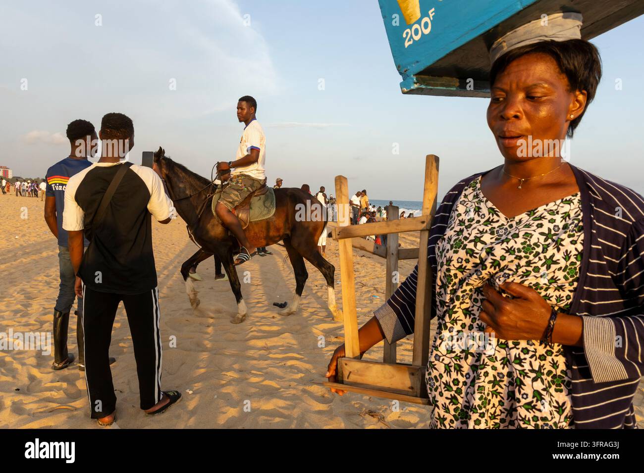 Homme montant un cheval le long du sable tandis que des spectateurs enregistrent avec un téléphone près d'un kiosque de bord de mer, Région Maritime, Lomé, Togo Banque D'Images