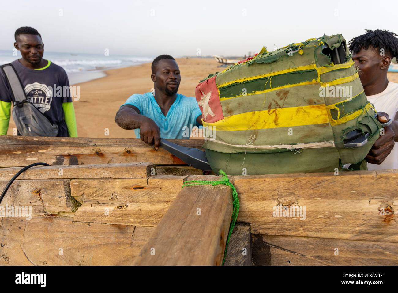 Pêcheurs debout à côté d'un bateau en bois dont la proue est recouverte d'un tissu cousu aux couleurs du drapeau du Togo, Région Maritime, Lomé, Togo Banque D'Images