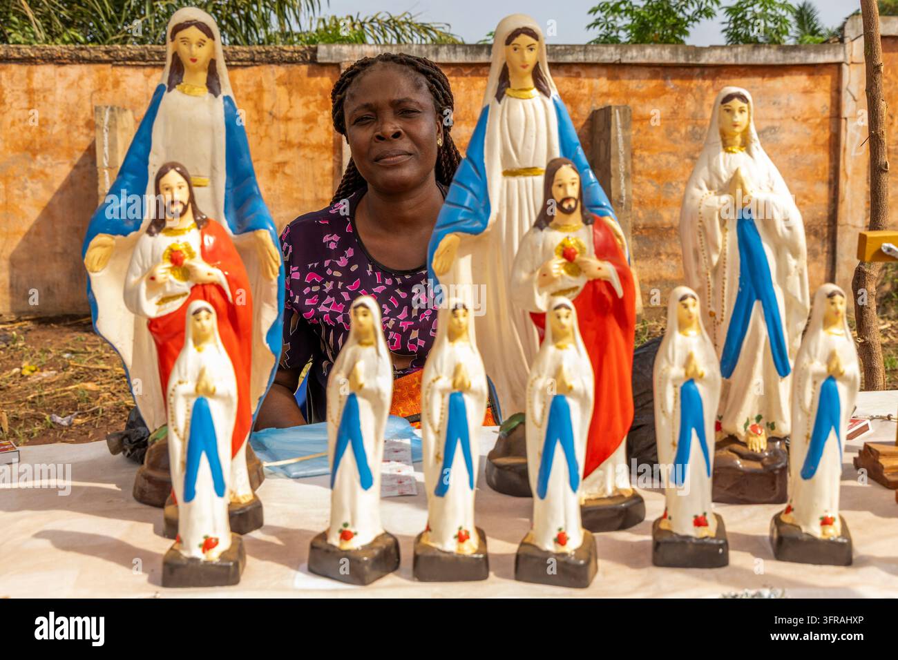 Femme vendant des statues religieuses de Jésus et de la Vierge Marie à un étal de marché, région maritime, Togoville, Togo Banque D'Images