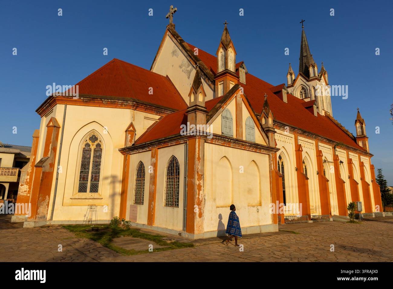 Une femme passe devant une grande église de l'ère coloniale avec un toit rouge et un clocher élevé, région des Plateaux, Kpalime, Togo Banque D'Images