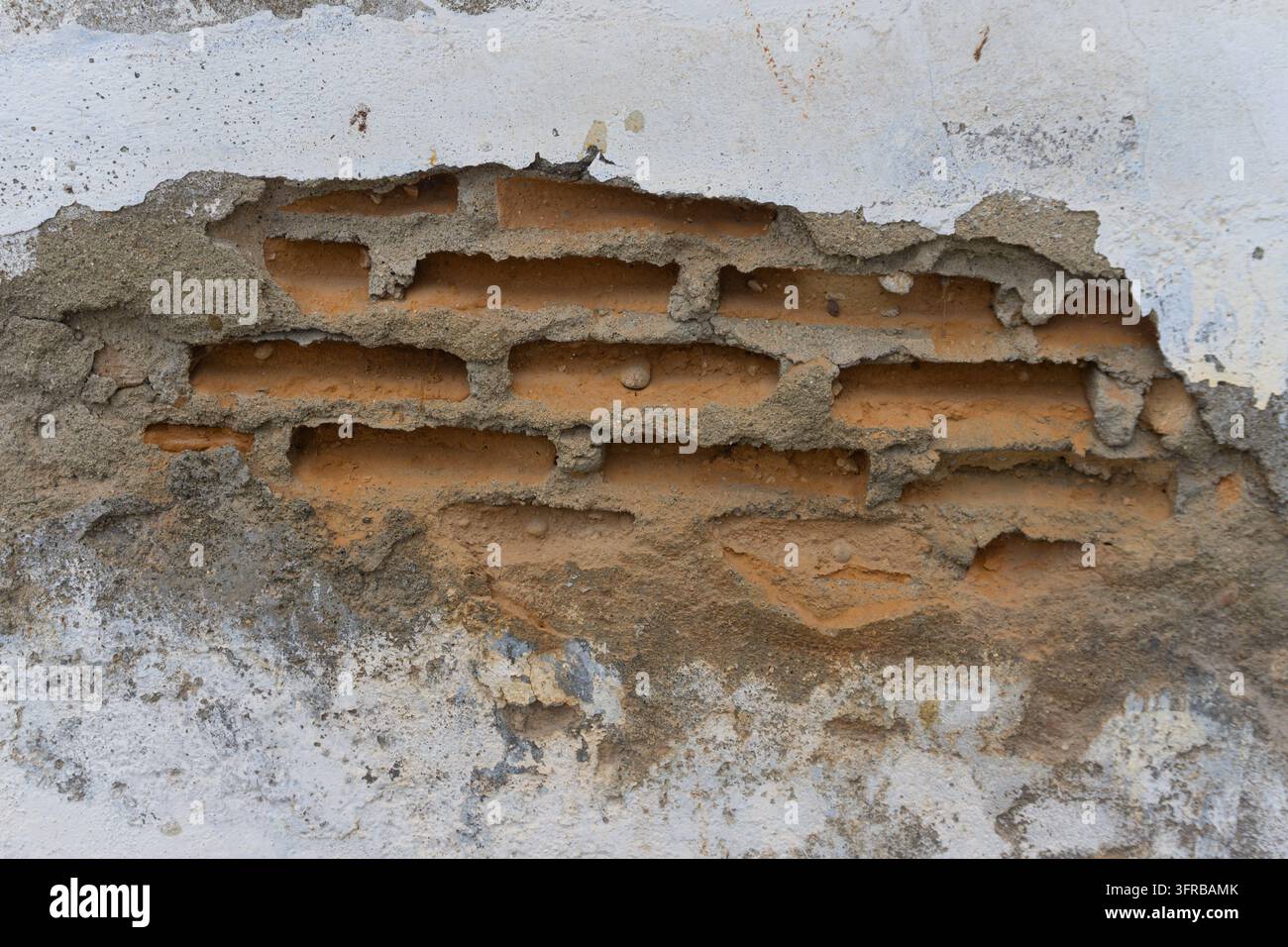 Mur endommagé montrant les couches de briques où le plâtre s'est détaché, fond texture grunge en plein cadre Banque D'Images