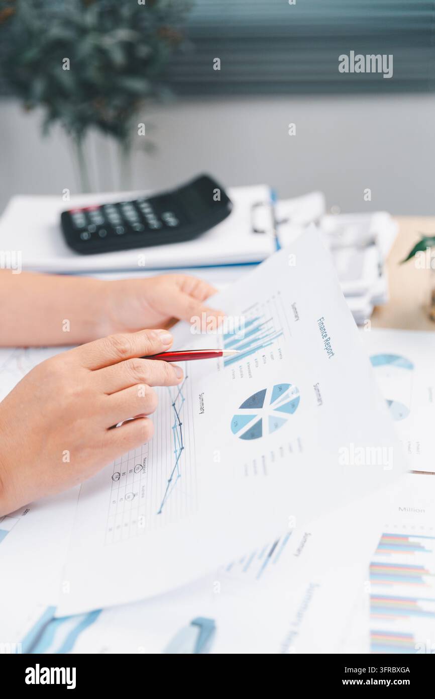 Professionnel d'affaires examinant des rapports financiers avec des graphiques et un stylo à un bureau, représentant la comptabilité, l'audit, l'analyse de données, le budgétisation, p Banque D'Images