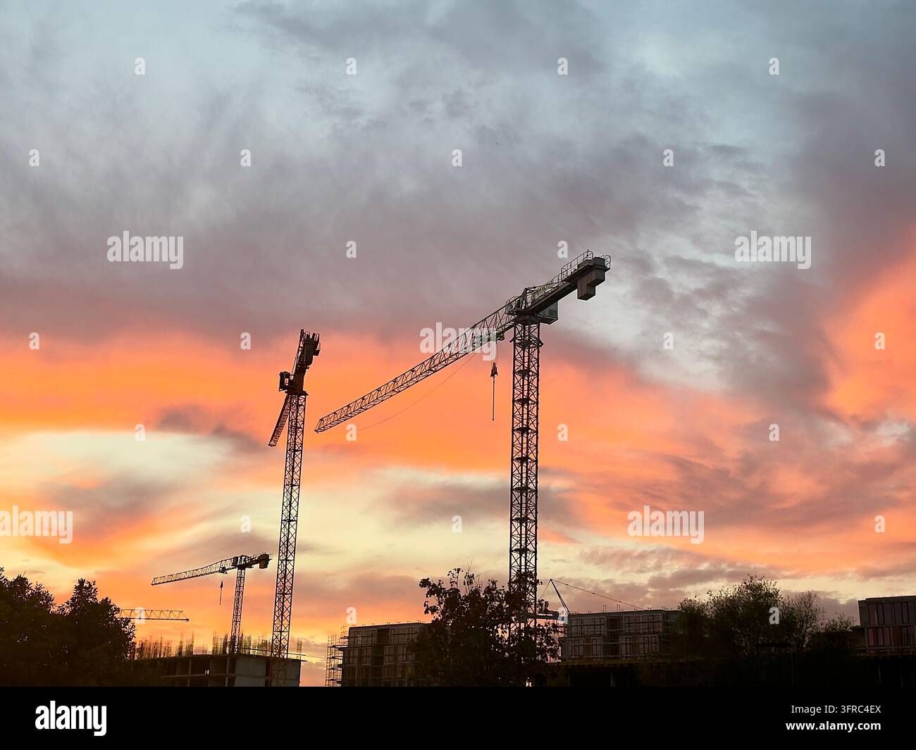 Silhouette d'une grue industrielle sur un chantier de construction contre un ciel dramatique orangé flamboyant au coucher du soleil à Bourgas. - Image de stock capturée avec un smartphone