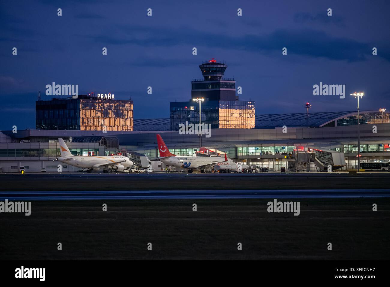 Avion de ligne garé au terminal de l'aéroport de Prague sous la tour de contrôle et les bâtiments de l'aéroport illuminés pendant l'heure bleue. Banque D'Images