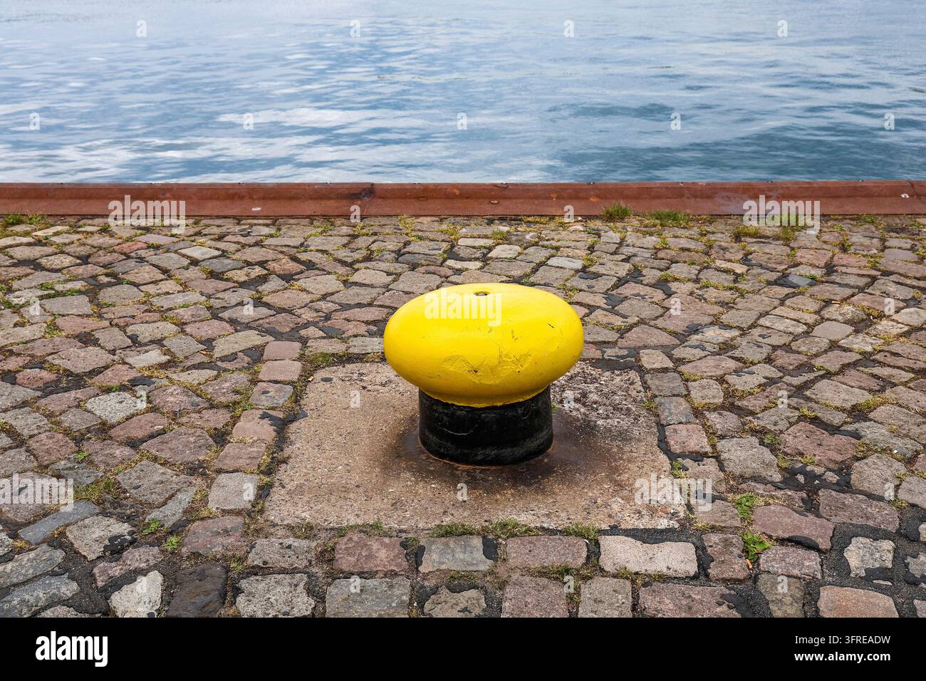 Borne d'amarrage jaune debout sur la jetée pavée au bord de la mer, fournissant un point d'amarrage sûr pour les bateaux et les navires Banque D'Images
