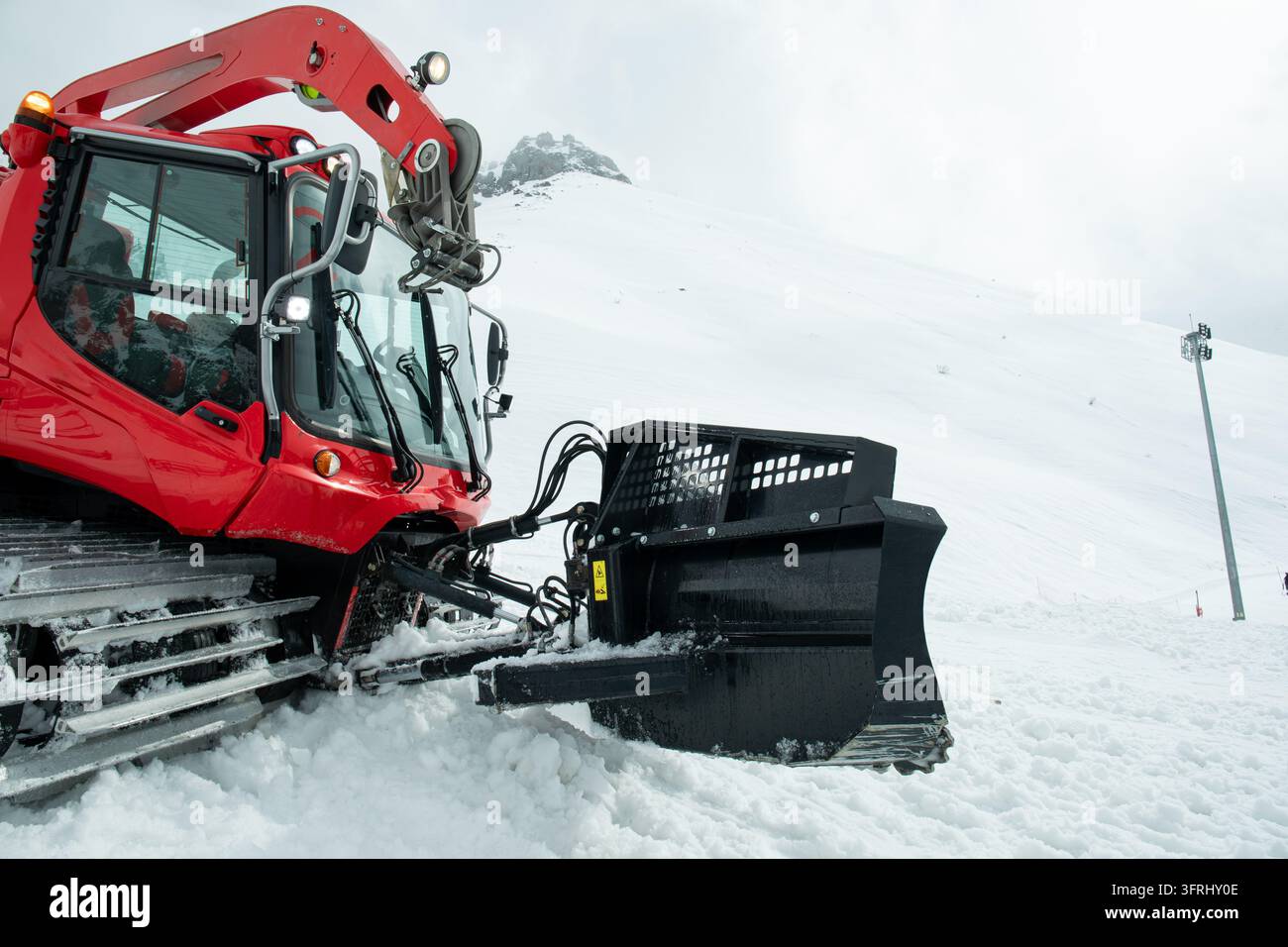 Véhicule de nivellement de neige opère sur un paysage montagneux enneigé, façonnant le terrain pour les skieurs. Banque D'Images