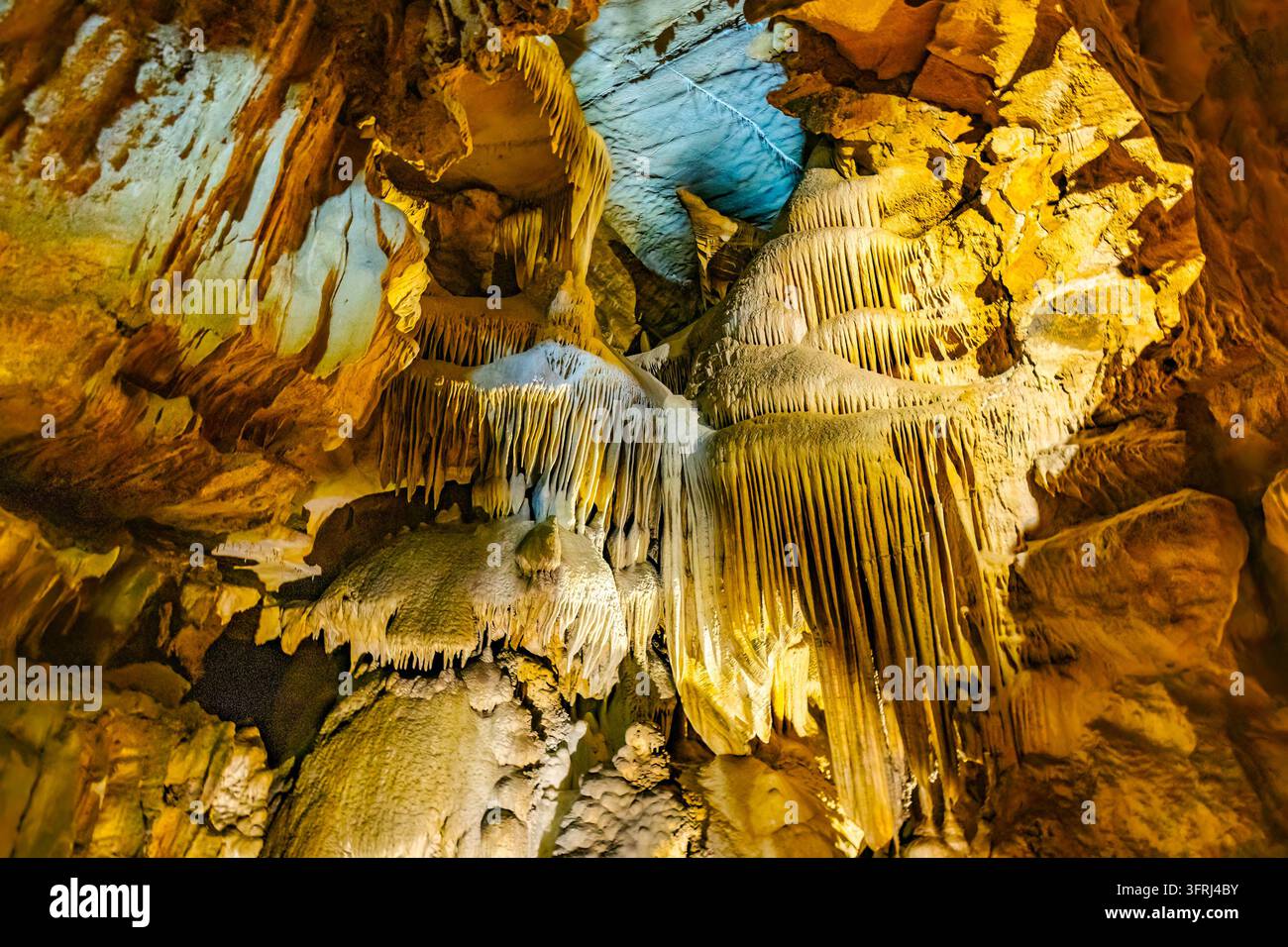 Un éclairage bleu et or vif illumine des formations de draperie dramatiques à l'intérieur de la grotte de cristal Banque D'Images