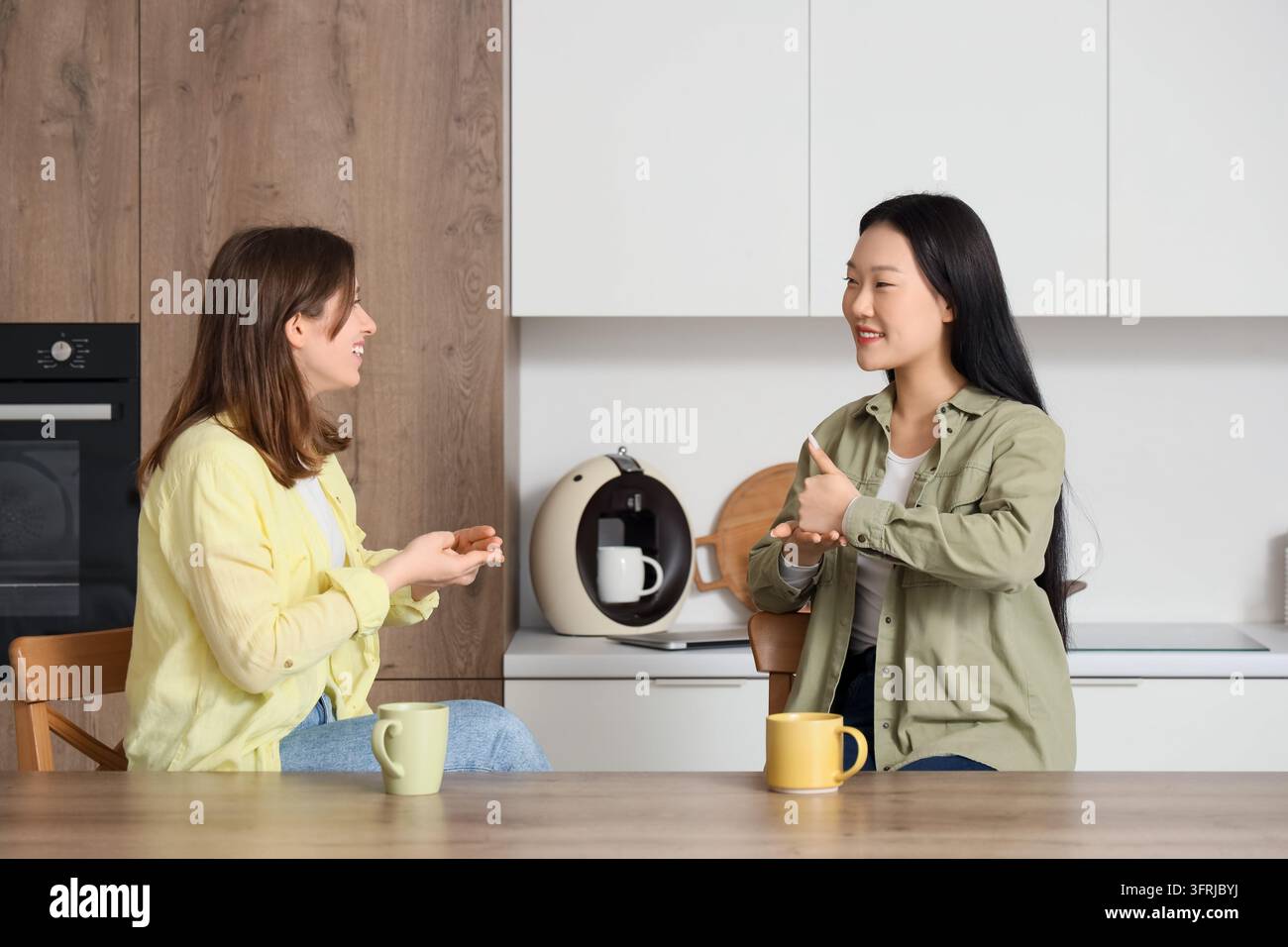 Inclusion et accessibilité, deux jeunes femmes communiquant en langue des signes dans une cuisine moderne, culture sourde et communication non verbale Banque D'Images