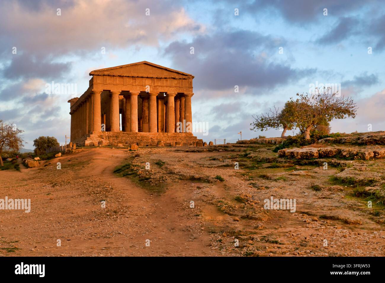 Le temple grec dorique du Ve siècle av. J.-C. est éclairé par le soleil hivernal en fin d'après-midi sous un ciel nuageux dans le parc archéologique d'Agrigente, Sicile, Italie Banque D'Images