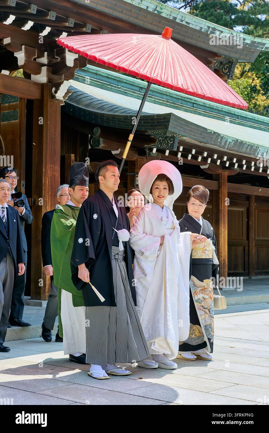 Mariée en kimono shiromuku blanc et marié en hakama marchent sous un parapluie en papier rouge avec un prêtre et des proches lors d'une cérémonie traditionnelle Banque D'Images