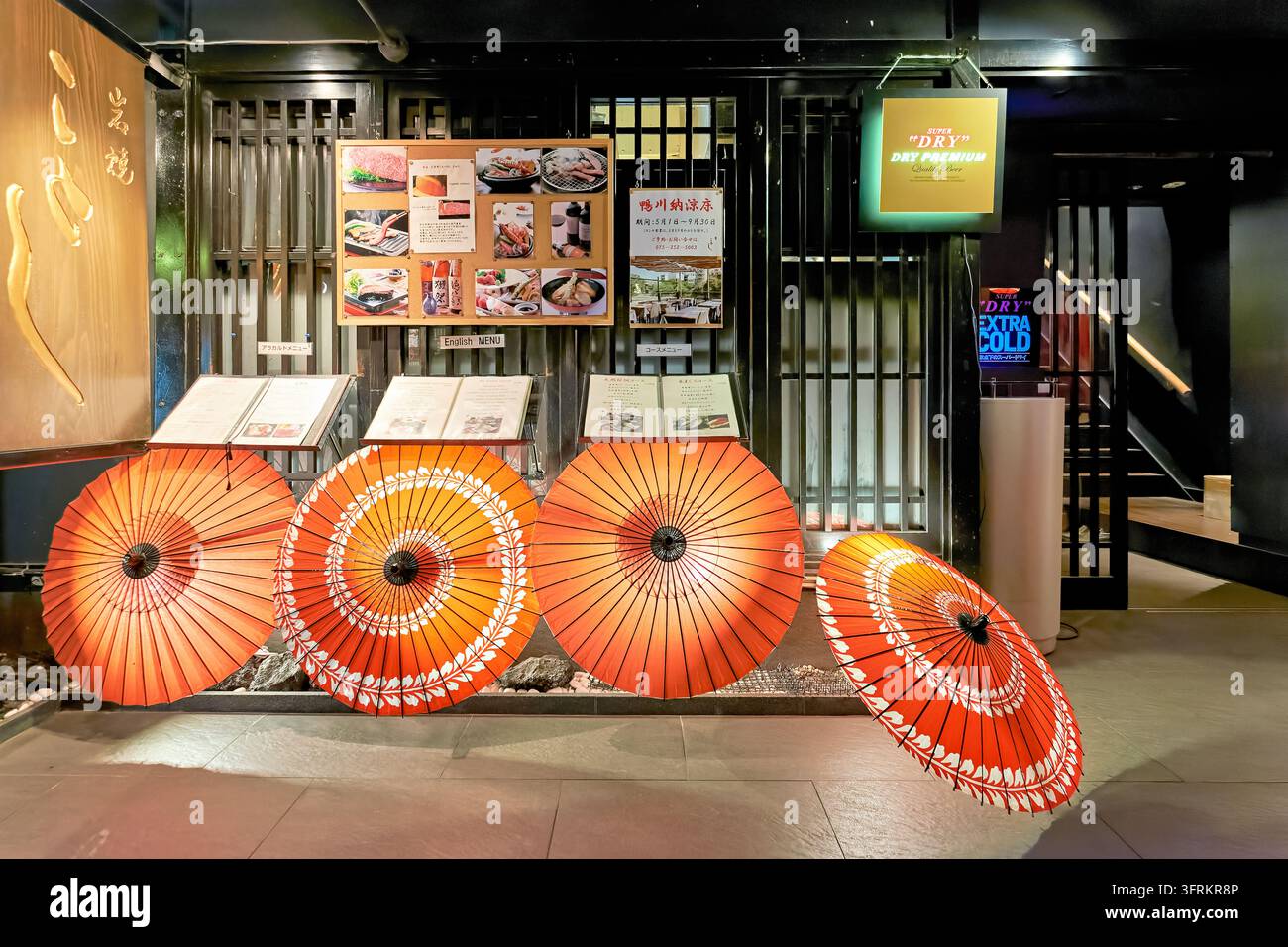 Des parasols orange wagasa et des tableaux de menu décorent la vitrine d'un restaurant au grill de pierre iwayaki à Kyoto, Japon, la nuit au printemps Banque D'Images